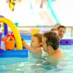 Un bébé joue avec des jouets dans l'eau tenue par son père