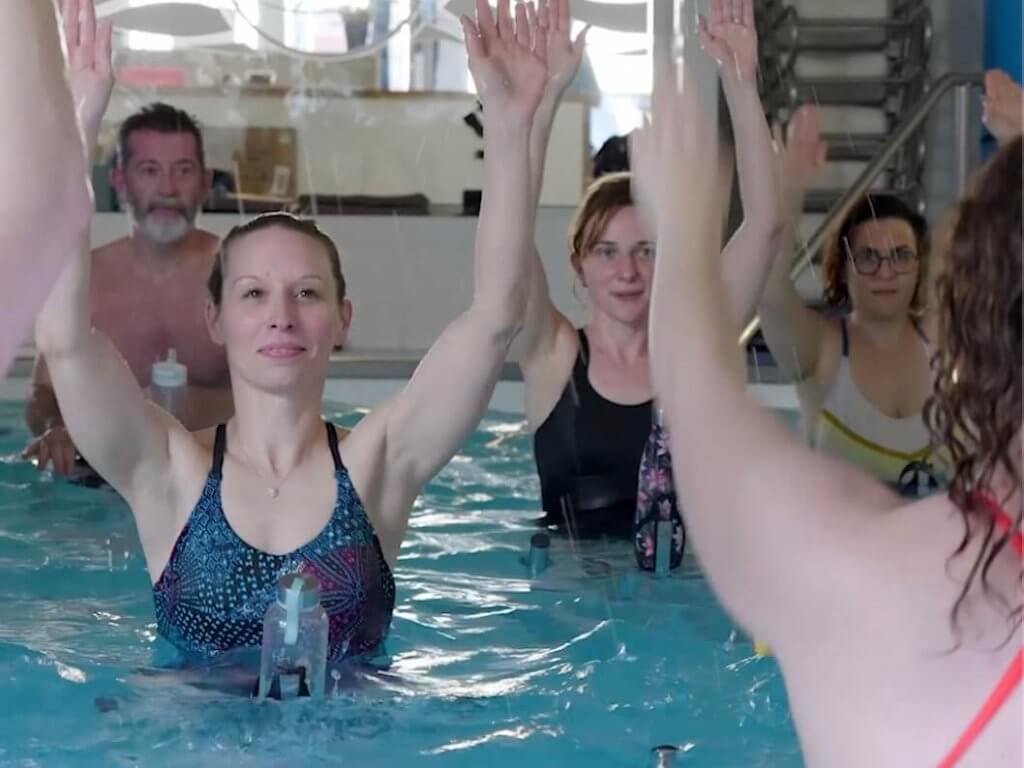 Plusieurs personnes lève les mains pendant un cours d'aquabike